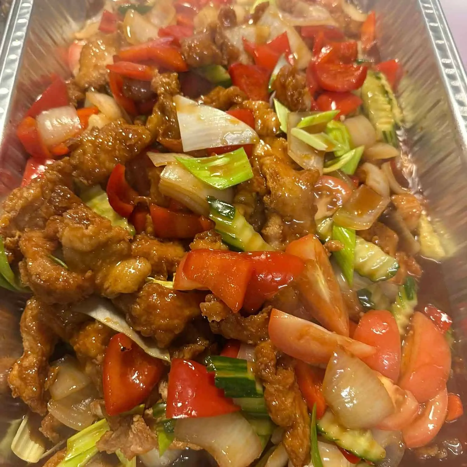 Fritert svinekjøtt med grønnsaker i saus, servert i aluminiumsform.