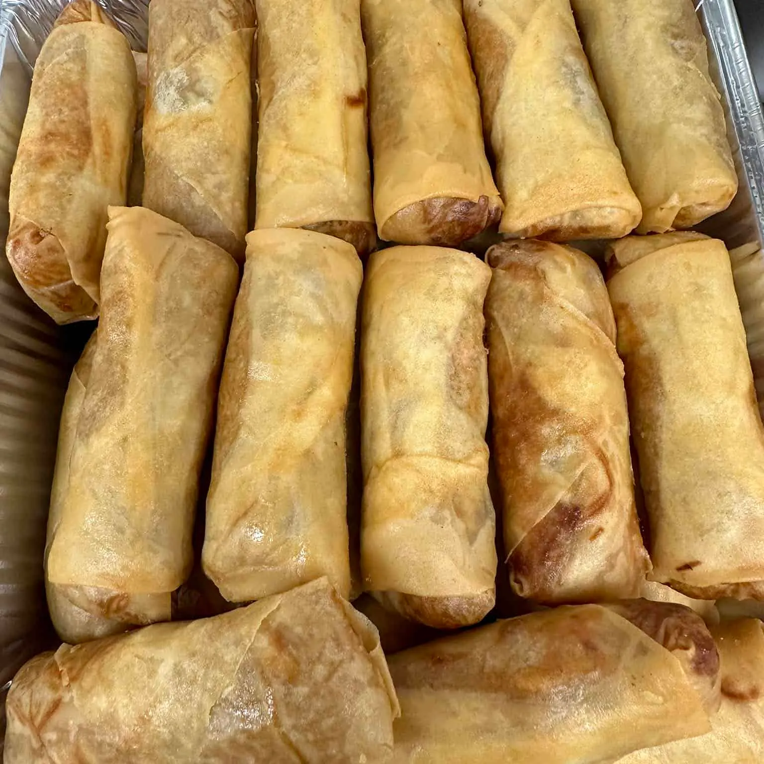 Aluminiumsform med rad på rad av gyllenstekte vårruller klare til servering.