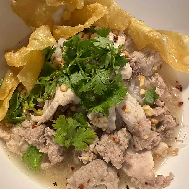 Lys suppe med strimlet svinekjøtt, koriander og friterte chips i dyp skål.