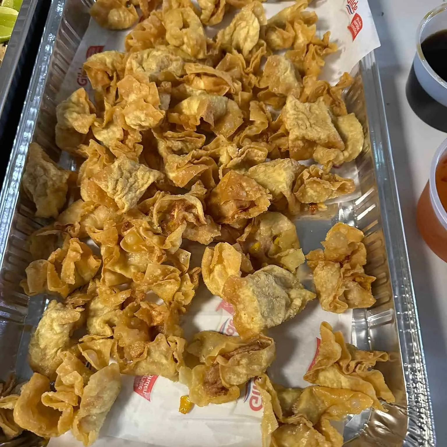 Aluminiumsform fylt med sprøstekte wontons i ujevn fasong, klare til servering.