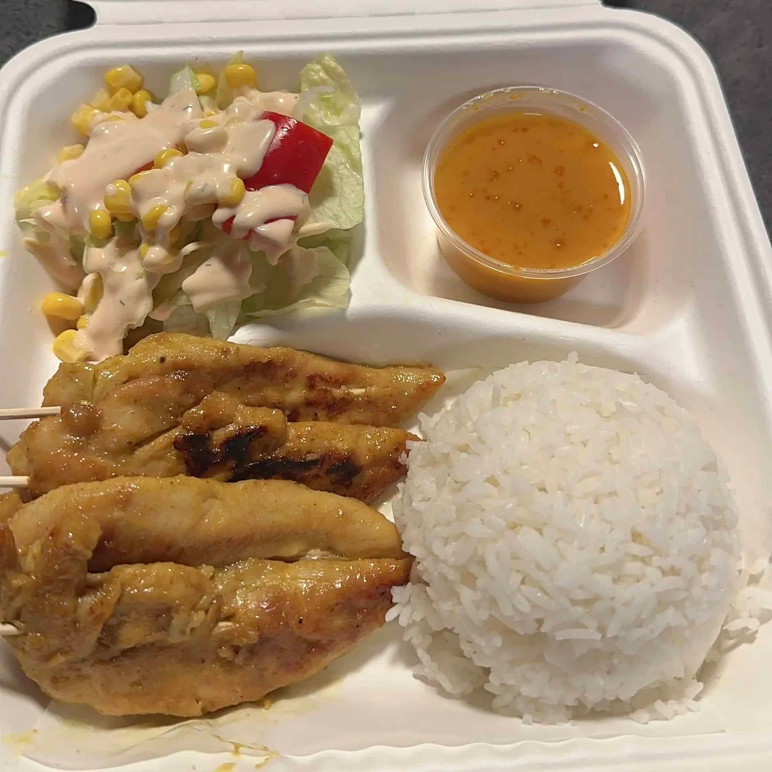Kyllingsatay med ris, salat og peanøttsaus i hvit take-away-boks.
