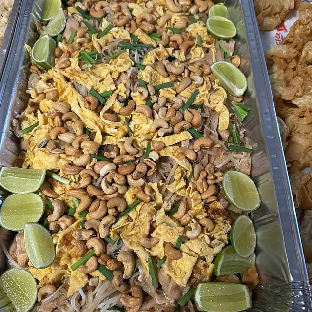 Nudelrett med cashewnøtter, eggebiter, limebåter og friske urter i aluminiumsform.